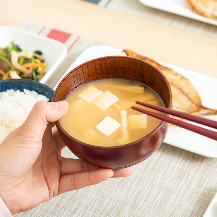 味噌汁を持ちながら食事を取っているイメージ画像