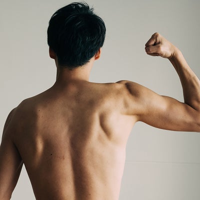 右腕を曲げ筋肉の盛り上がりを見せている男性の後ろ姿の画像