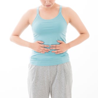 タンクトップ姿の女性が両手を腹部にあてている様子
