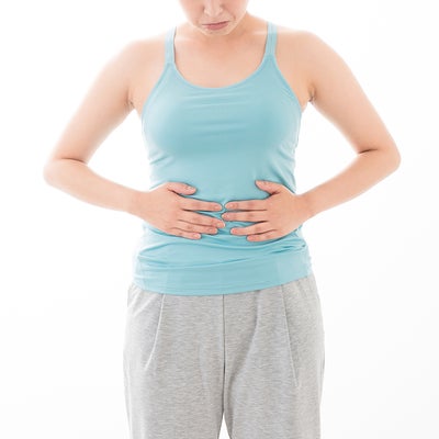 タンクトップ姿の女性が両手を腹部にあてている様子