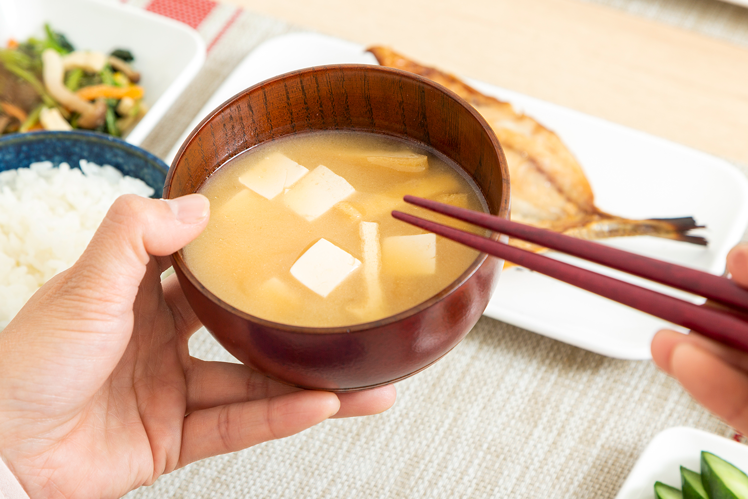 味噌汁を手に持ち和食を食べているイメージ画像