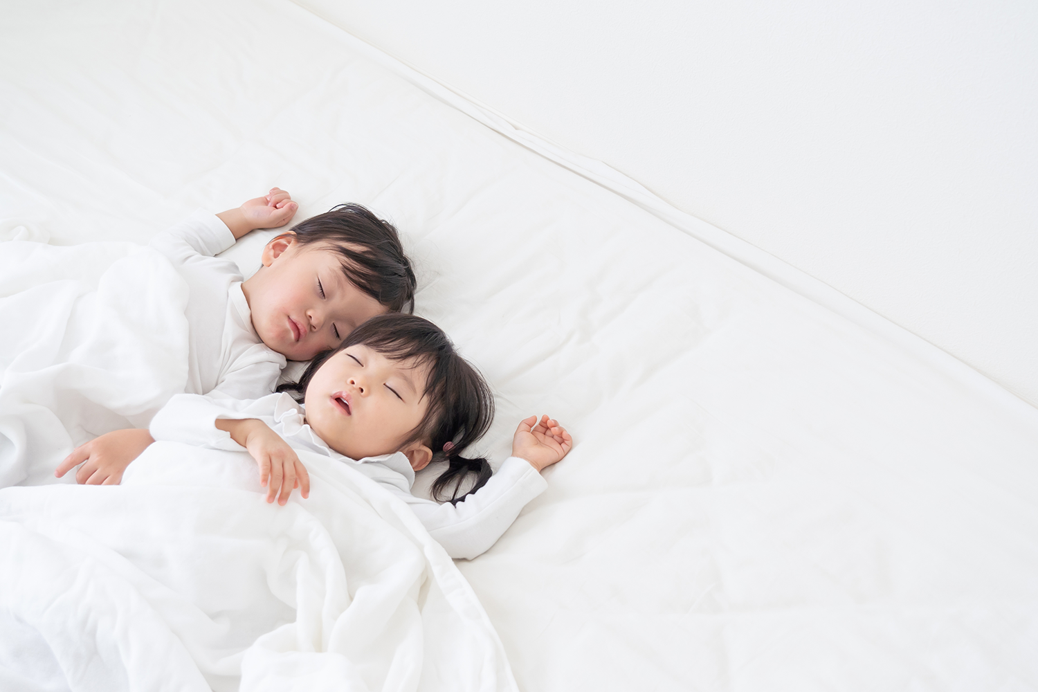 白い寝具で眠っている二人の子どもの画像